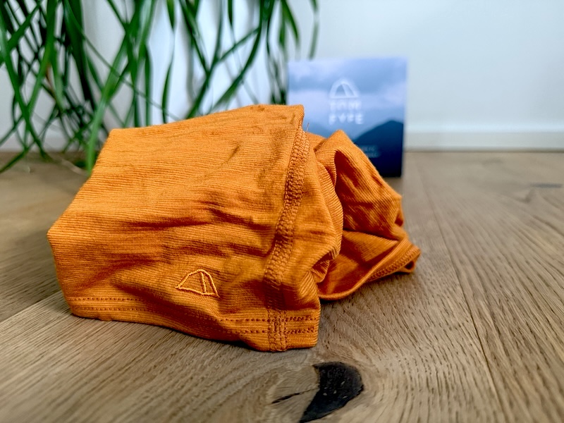 TOM FYFE Merino Schlauchschal – Detailansicht und Verarbeitung. TOM FYFE Merino Schlauchschal Kurkuma – Detailaufnahme des Logos und der Stoffstruktur